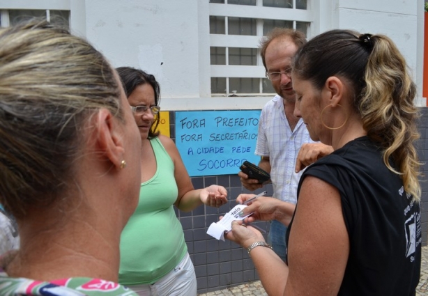 MIcaela, de blusa preta, com colegas, oferece um bilhete de rifa