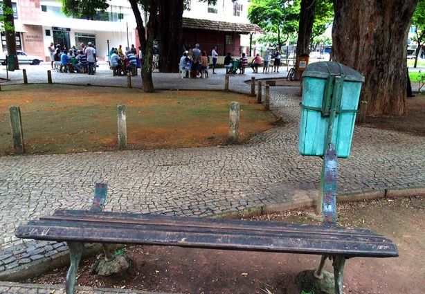 Um dos bancos em pior estado de conservação da praça, e atrás dele área que um dia foi gramada com uma lixeira velha