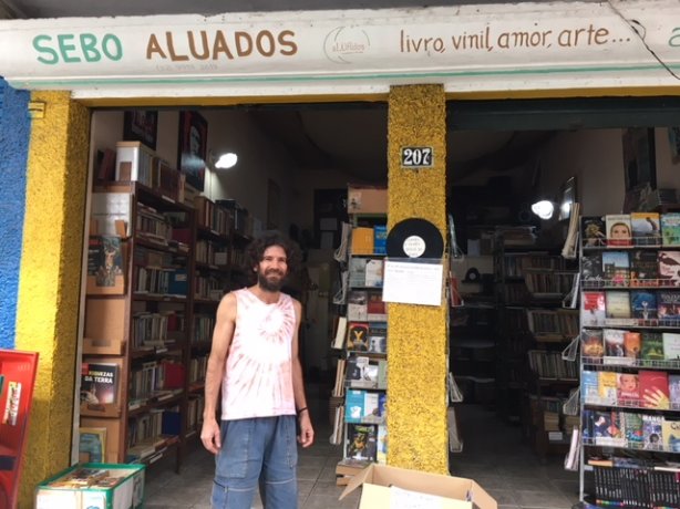 O professor mestre e propriet&aacute;rio do Sebo aLUAdos, Luciano de Andrade ao lado da banca de livros gratuitos